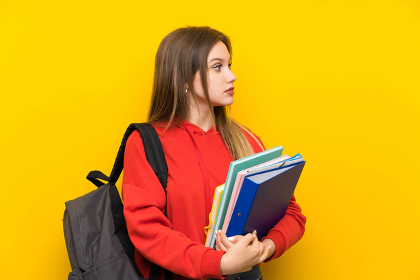Teenager student girl over yellow background looking side - Фото, изображение