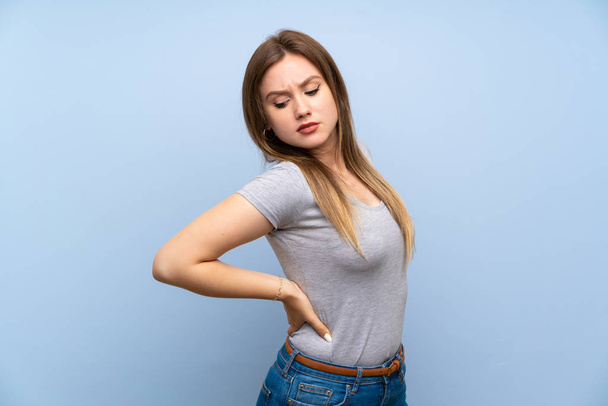 Tiener meisje over geïsoleerde blauwe muur die lijdt aan rugpijn voor het hebben van een inspanning - Foto, afbeelding