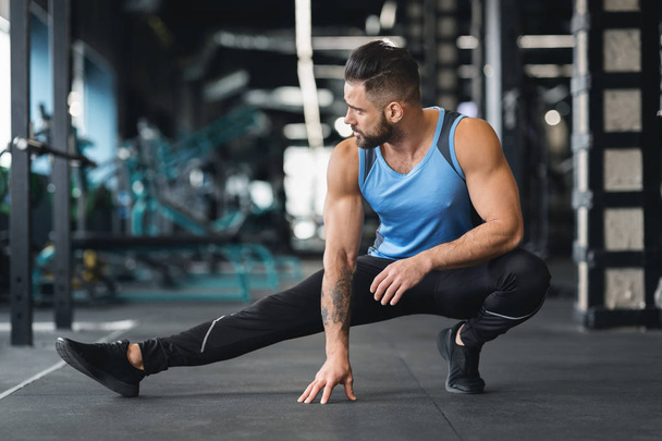 Spor salonunda sportif adam bacaklar için germe egzersizleri yapıyor - Fotoğraf, Görsel