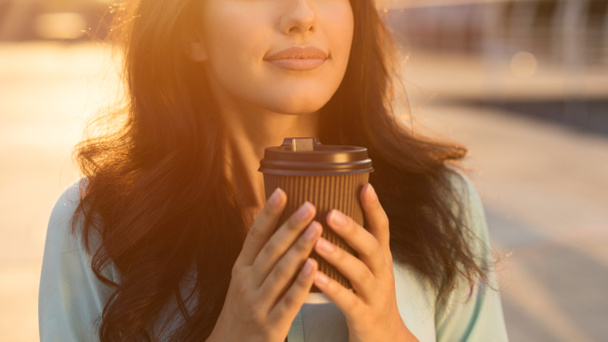 Girl smelling hot chocolate in takeaway cup, outdoors - Fotó, kép