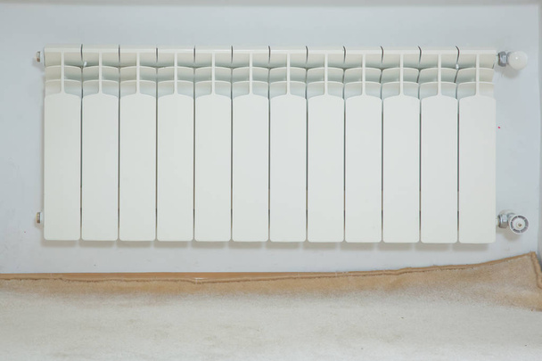 just installed a new steel heating radiator. Full view of a white radiator against a cream wall . Interior detail. White metal radiator on a white wall. Central heating radiator . - Foto, immagini