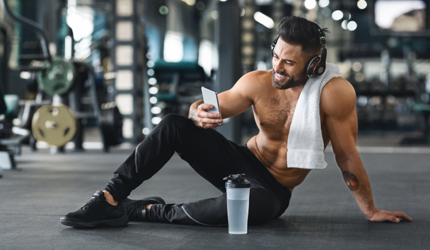 Muscular man using cellphone at gym, free space - Zdjęcie, obraz