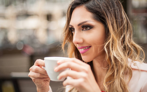 Portrait of woman sitting in outdoor cafe and drinking coffee - Foto, imagen