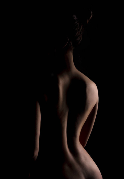 Graceful line of back of young naked woman on black background, - Photo, Image