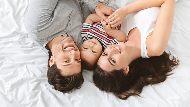 Adorable baby lying in bed with parents, having fun - Photo, Image