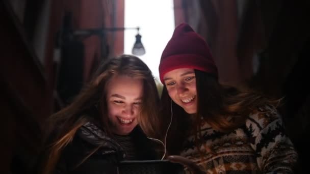 Two young smiling women walking on the street and looking at the phone screen with headphones - Materiał filmowy, wideo