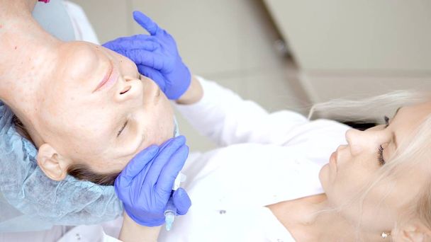 Der Kosmetologe führt Injektionen durch, Anti-Aging-Verfahren zur Straffung und Glättung von Falten auf der Gesichts- und Halshaut einer Frau. vertikal - Foto, Bild