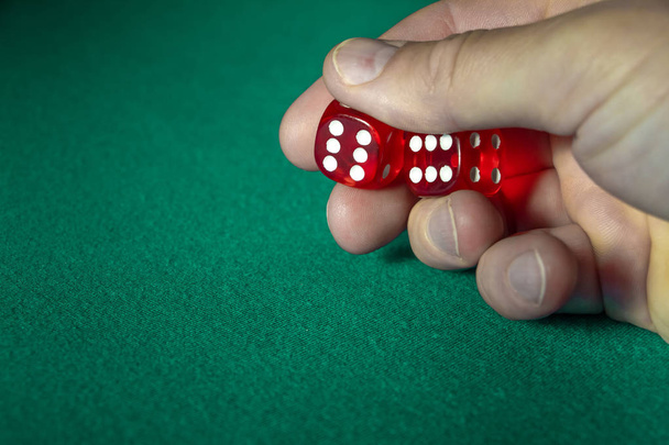 Κοντινό πλάνο, κρατώντας κόκκινα ζάρια με έναν νικηφόρο συνδυασμό σε πράσινο πανί σε ένα καζίνο. - Φωτογραφία, εικόνα