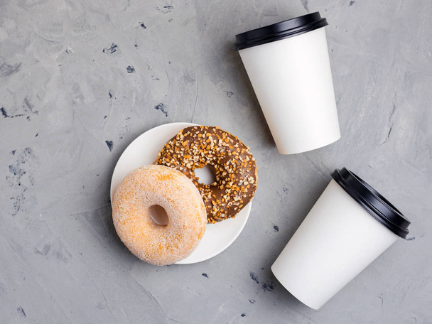 Donuts coloridos e copos de papel branco em fundo de concreto cinza, close-up, vista superior. Conceito de padaria, doces frescos, delicioso café da manhã, fast food
 - Foto, Imagem