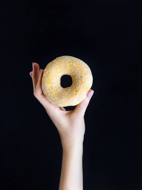 Woman hand hold sweet sugar donut on black background - Fotó, kép