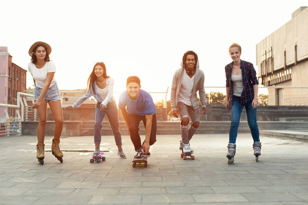 ローラースケートとスケートボードを持つ笑顔のティーンエイジャーのグループ - 写真・画像