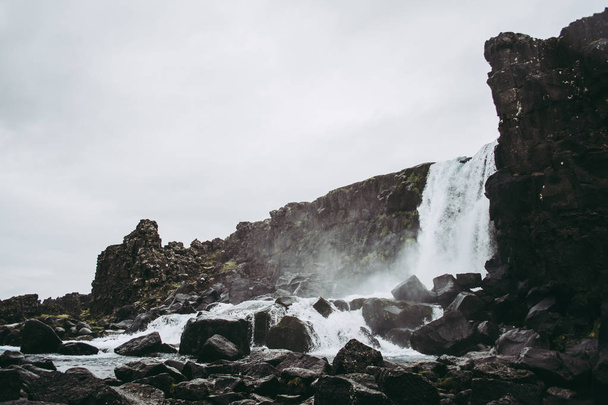La cascade dans le parc national de Thingvellir, Islande coulant dans la piscine remplie de roches. Météo nuageuse au printemps
 - Photo, image
