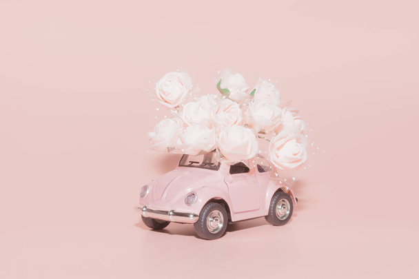 Pink retro toy car with bouquet of white Roses on pink background. Concept Valentine's day, February 14 card, 8 March, International Happy Women's Day - Foto, Imagem