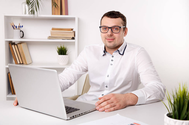 Бизнесмен в очках в офисе сидит перед ноутбуком
. - Фото, изображение