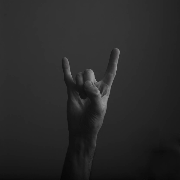 male devil horn rock and roll hand gesture against dark background - Photo, Image