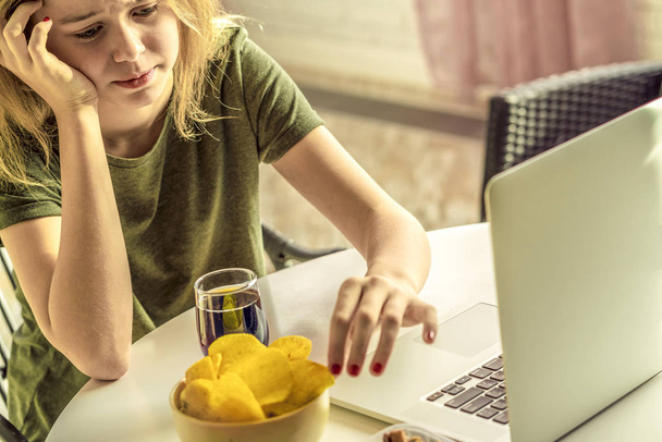 Meisje werkt op een computer en eet fast food. Ongezond eten: chips, crackers, snoep, wafels, Cola. Junk food, concept. - Foto, afbeelding