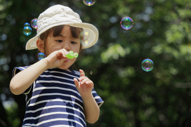 Японская девочка, играющая с мыльным пузырем под голубым небом (4 года)
) - Фото, изображение