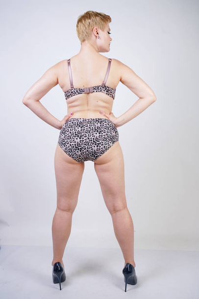 Beautiful young caucasian chubby woman with plus size body and pale skin wearing sexy lingerie with leopard print on white studio background alone - Valokuva, kuva