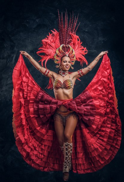 赤い羽の衣装を着た才能ある喜びのダンサーが小さな暗いスタジオでポーズをとっている. - 写真・画像