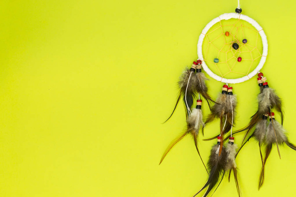 Dreamcatcher with brown bird feathers, and with threads and beads of rope hanging. Dreamcatcher handmade. Lies on a green background. - 写真・画像