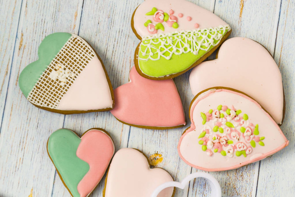 Pink and colored gingerbread and honey cakes and heart-shaped cookies lie in a messy pile on a light wooden background. Nearby are white molds for baking. Place for text. The concept of love, mother's - Foto, imagen