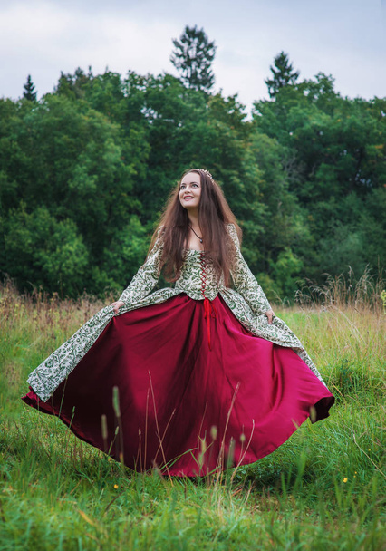 Kaunis onnellinen nainen keskiaikaisessa mekossa tanssia ulkona
 - Valokuva, kuva