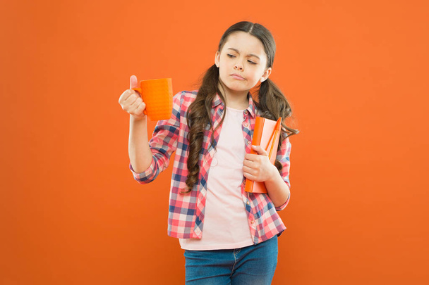 This is not my cup of tea. Dissatisfied girl looking at cup during lunch on orange background. School child having lunch break. Small girl at school lunch. Little kid drinking tea or milk for lunch - Photo, image
