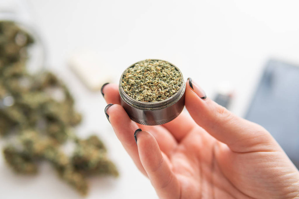 fresh weed marijuana in grinder in wooman hand, Cannabis buds on white table, close up - Foto, afbeelding