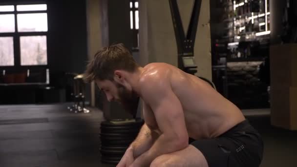 Closeup shoot of adult muscular athletic shirtless man sitting and resting after workout indoors in the gym - Filmagem, Vídeo