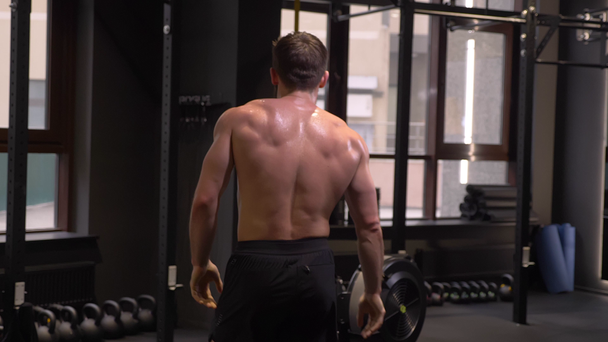 Closeup back view shoot of adult muscular athletic man making squats with the kettlebells indoors in the gym - Materiał filmowy, wideo