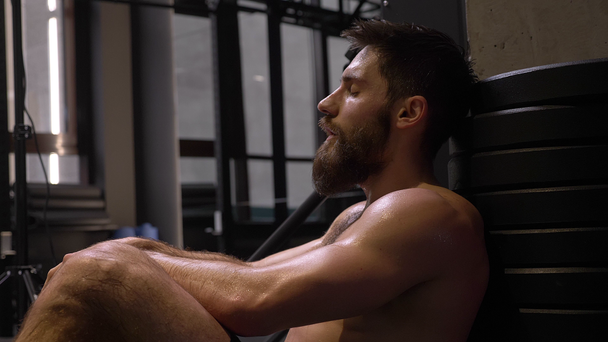 Closeup hajtás felnőtt izmos sportos ember ül, és hogy fáradt beltéri az edzőteremben - Felvétel, videó
