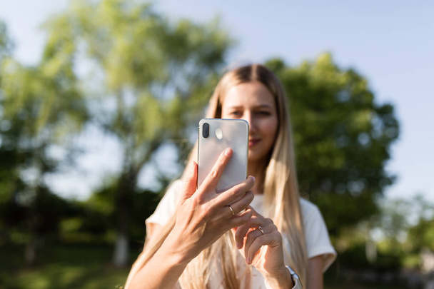 Beautiful young woman with blonde hair using mobile phone outdoor. Stylish girl making selfie - Foto, afbeelding