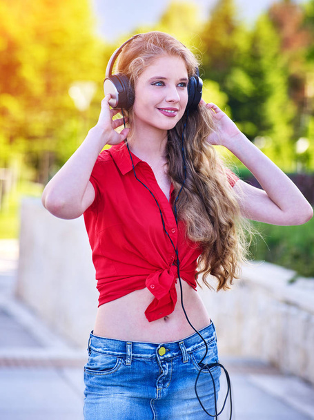 Mädchen in Kopfhörer und Jeans hört Musik mit geschlossenen Augen - Foto, Bild