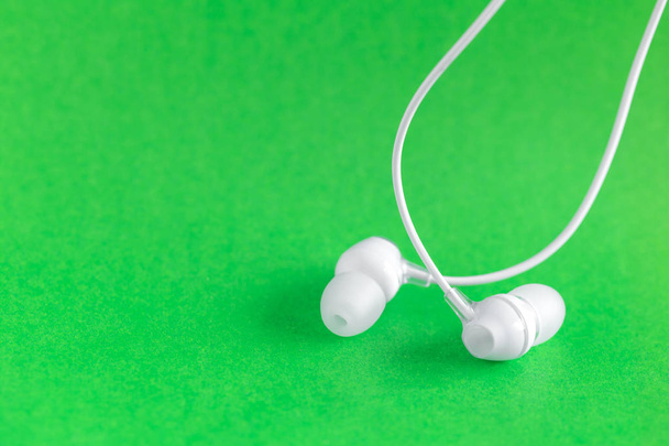 Λευκά ακουστικά σε πράσινο πολύχρωμο φόντο με αντίγραφο χώρο για το κείμενο - Φωτογραφία, εικόνα