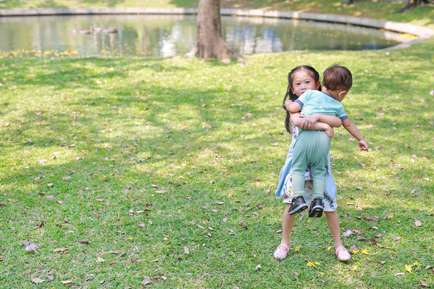 Asian sister carrying her little brother in the garden outdoor. - Foto, Imagen