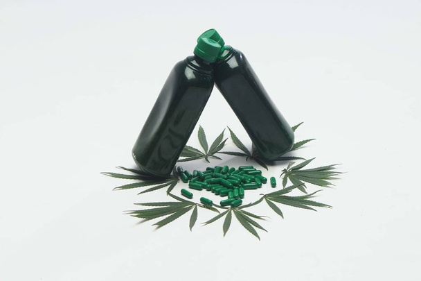 Koristelu marihuanan lehdet alla ayurvedic lääke vihreä pullo. Ayurvedic vihreät tabletit eristetty valkoisella taustalla
. - Valokuva, kuva
