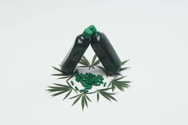 Dekoracja liści marihuany poniżej medycyny ajurwedyjskiej zielonej butelce. Ayurvedic zielone tabletki izolowane na białym tle. - Zdjęcie, obraz