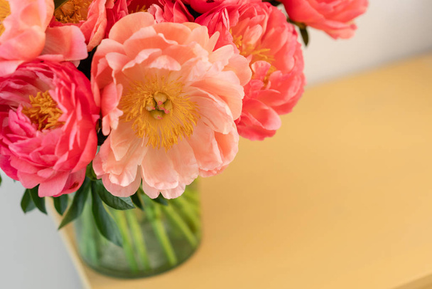 木製のテーブルの上のガラスの花瓶の中のサンゴの孔子.カタログやオンラインストアのための美しいピオニーの花。フローラルショップコンセプト.美しい新鮮なカットブーケ。花の配達。スペースのコピー - 写真・画像