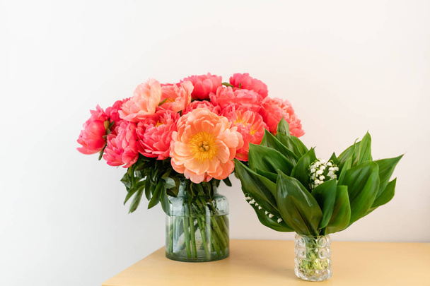 木製のテーブルの上のガラスの花瓶の谷のサンゴのピオニーと春のユリ.カタログやオンラインストアのための美しいピオニーの花。フローラルショップコンセプト.美しい新鮮なカットブーケ。花の配達. - 写真・画像