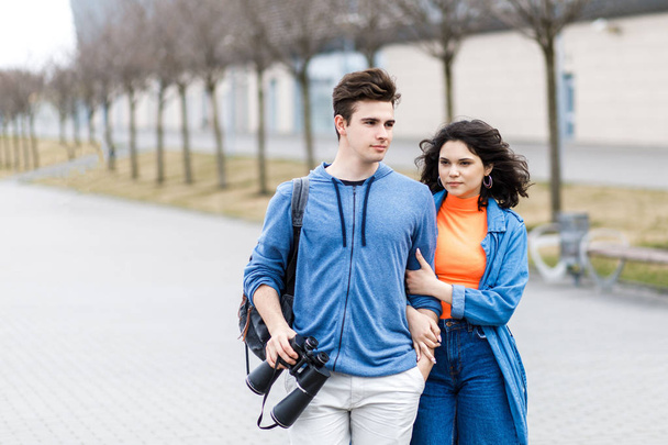 Ένα νεαρό όμορφο ζευγάρι - ένα αγόρι και ένα κορίτσι που περπατούν στην πόλη με ένα κιάλια στα χέρια του. Οι νέοι ταξιδεύουν. - Φωτογραφία, εικόνα