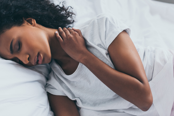 attraktive afrikanisch-amerikanische Frau leidet unter Nackenschmerzen, während sie mit geschlossenen Augen im Bett liegt - Foto, Bild