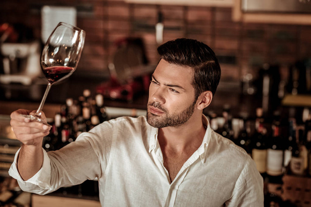 Genç esmer adam bir bardak şaraba bakıyor. - Fotoğraf, Görsel