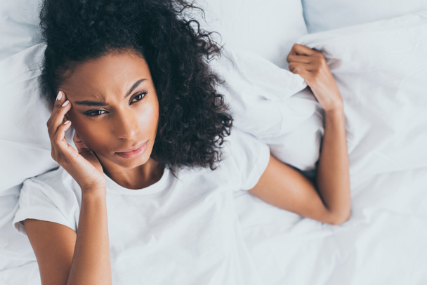 upset african american woman suffering from headache while lying in bed - Valokuva, kuva