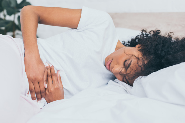 exhausted african american woman suffering from stomach pain while lying in bed - Photo, Image