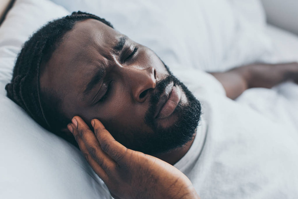 uitgeput Afro-Amerikaanse man lijdt hoofdpijn terwijl liggend in bed - Foto, afbeelding
