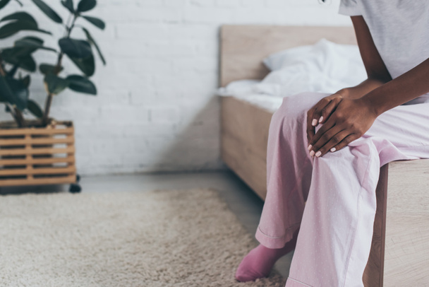 cropped view of african american woman suffering from knee pain while sitting on bed - Foto, Bild