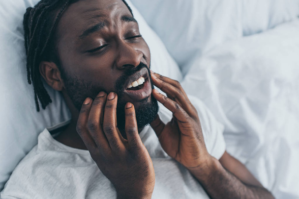 giovane uomo africano americano che soffre di dolore alla mascella in camera da letto
 - Foto, immagini