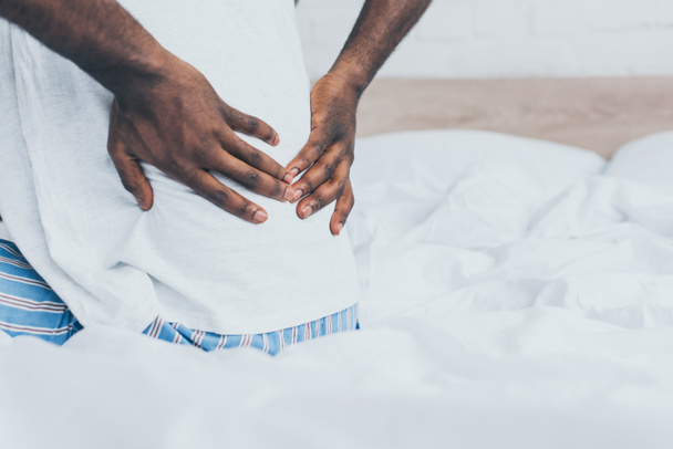 abgeschnittene Ansicht eines an Rückenschmerzen leidenden afrikanisch-amerikanischen Mannes im Schlafzimmer - Foto, Bild
