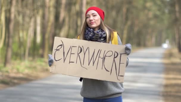 Fiatal csinos stoppos nő áll az úton plakáttal mindenhol  .  - Felvétel, videó