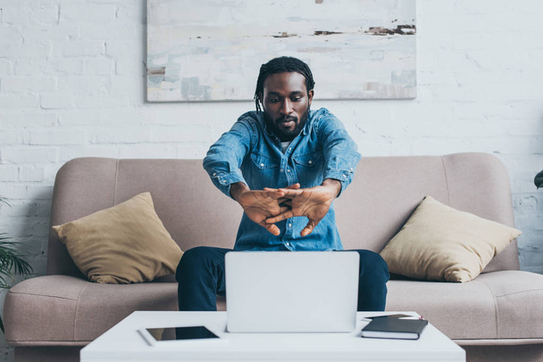 handsome african american man sitting on sofa near table with digital devices - Foto, Bild